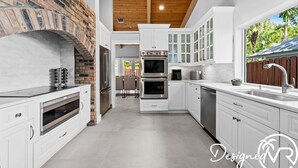 A modern kitchen with white cabinetry, a brick accent wall, and a wooden ceiling. - Charming 9BR New-build Home w/ Heated Pool & Games (Hollywood)