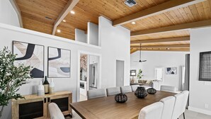 A modern dining area with a wooden table, white chairs, and abstract art on the walls. - Charming 9BR New-build Home w/ Heated Pool & Games (Hollywood)
