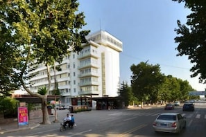 Hotel de diverses plantes amb façana plana, entrada coberta i vista al carrer amb cotxes i una moto.