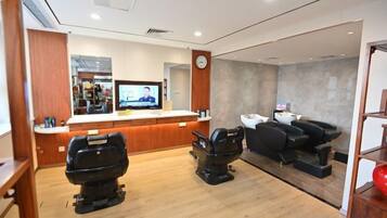 Un salon comprenant un comptoir d’accueil, deux fauteuils de massage et un écran de télévision.