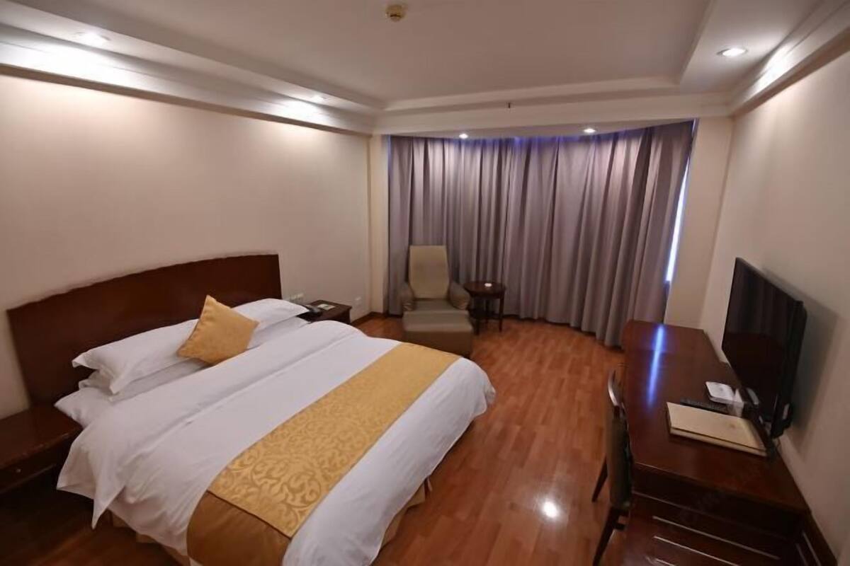 Una habitación de hotel con una cama grande, un escritorio con televisión y una silla.