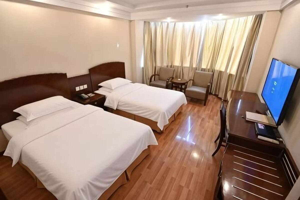 Habitación de hotel con dos camas, un escritorio con computadora, una silla y un televisor.