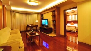 A hotel room with a sofa, a TV, a small table with items, a bed, and a wooden floor. - Xinda Hotel (Zoucheng)
