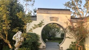 An arched entrance with a plaque, surrounded by greenery and a stone pathway. - Xinda Hotel (Zoucheng)