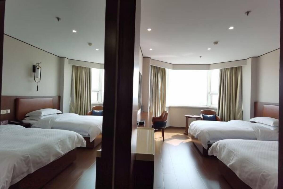 Habitación de hotel con dos camas, un escritorio, una silla y un amplio ventanal con cortinas.