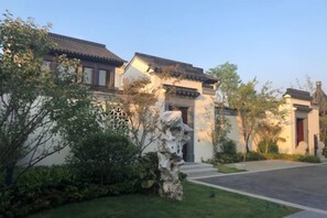 A traditional building with a tiled roof, a stone pathway, and a well-maintained lawn. - Xinda Hotel (Zoucheng)