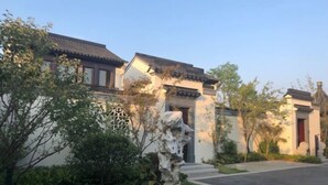 A traditional building with a tiled roof, a stone sculpture, and a well-maintained garden. - Xinda Hotel (Zoucheng)