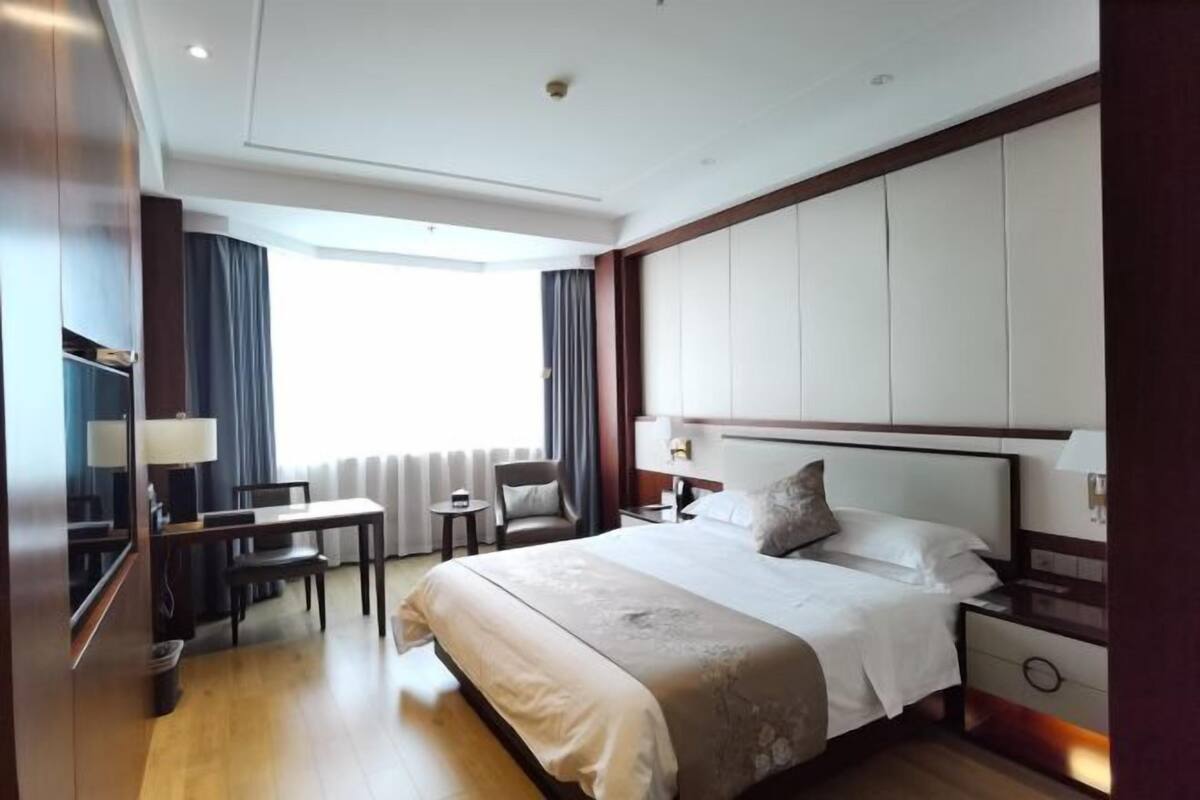 Una habitación de hotel con una cama grande, un escritorio, una silla y una ventana con cortinas.