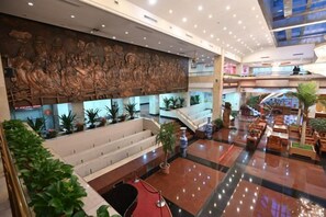 A hotel lobby with a large mural, a staircase, and a seating area with plants. - Xinda Hotel (Zoucheng)