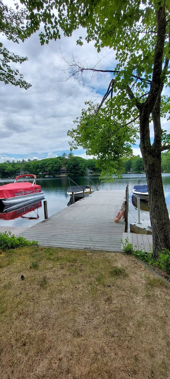 A wooden dock extending into a calm lake with boats docked on the left. - Cottage with great beach. (Wolfeboro)
