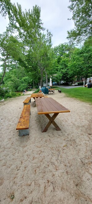 Ein Picknickplatz mit Holzbänken und -tischen, umgeben von Bäumen und einer Wiese.