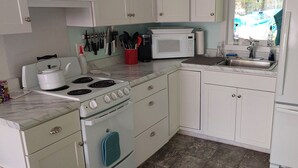 Una cocina pequeña con estufa, microondas, lavabo y armarios.