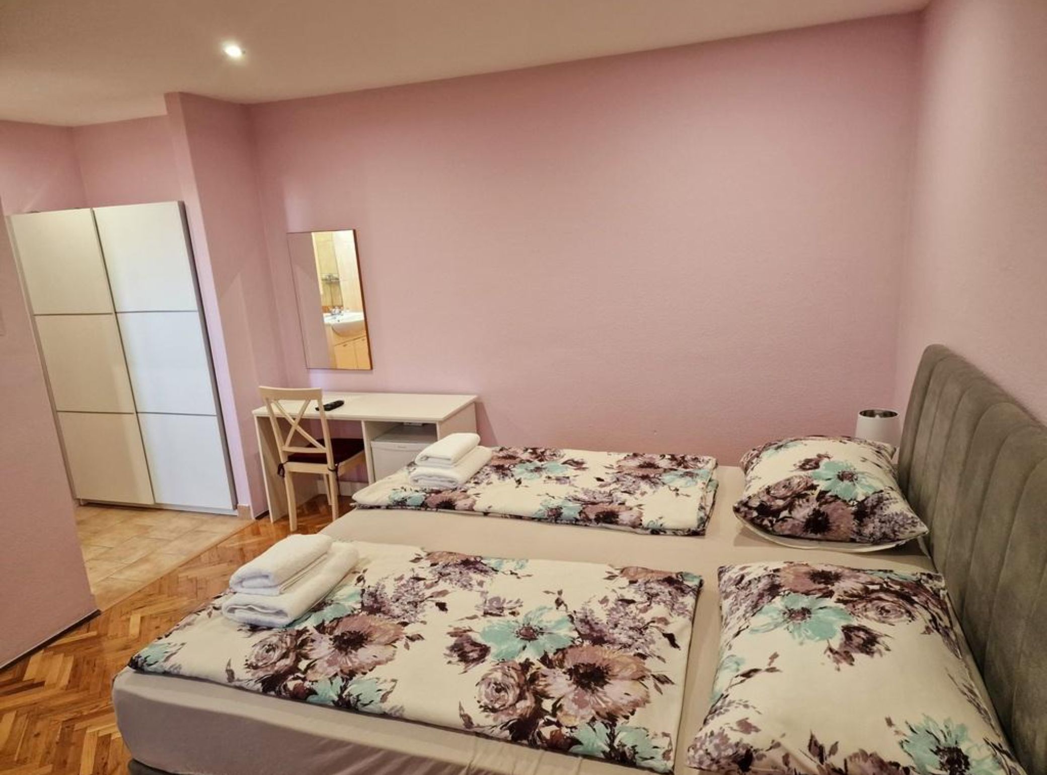 A bedroom with two beds, a desk, a chair, and a wardrobe.