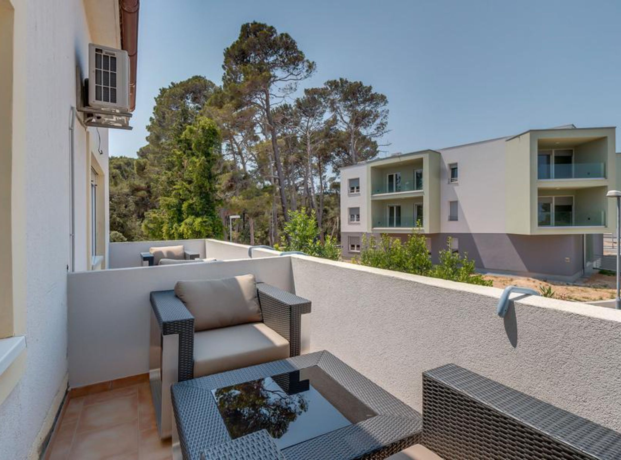 A balcony with outdoor furniture, including a sofa and a table, overlooking a residential area with trees and modern buildings.