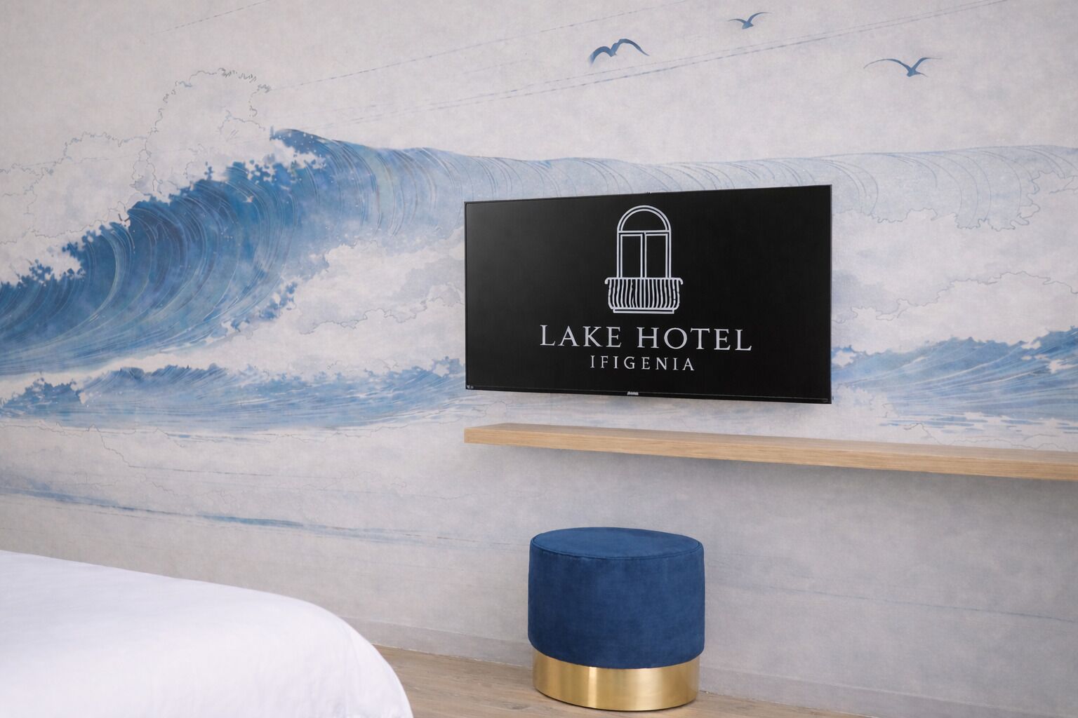 Placa na parede para o Hotel Lake em Ifigenia, uma prateleira de madeira abaixo e um banquinho azul.