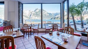 A restaurant with tables and chairs, large windows with a view of the sea and mountains, and a tiled floor. - Lake Hotel Ifigenia (Nago-Torbole)