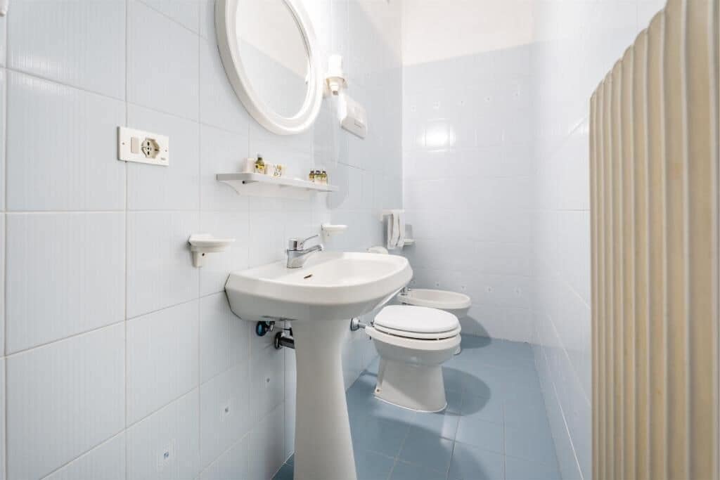 A modern bathroom with a pedestal sink, a toilet, and a mirror.