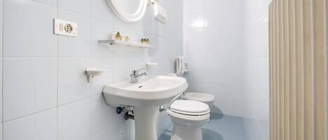 A modern bathroom with a pedestal sink, a toilet, and a mirror.