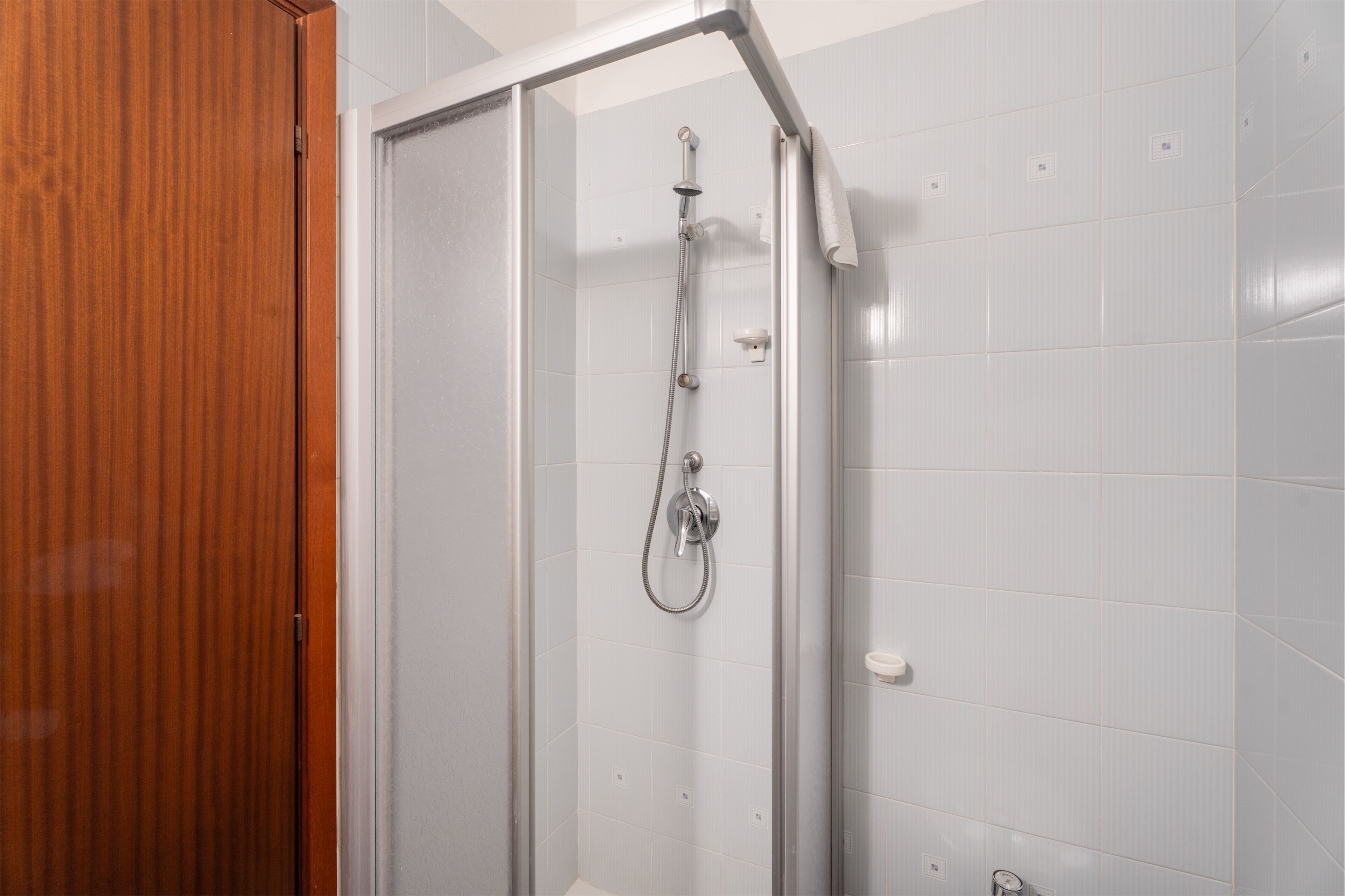 A shower with a glass door, white tiled walls, and a wooden door frame.