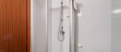 A shower with a glass door, white tiled walls, and a wooden door frame.