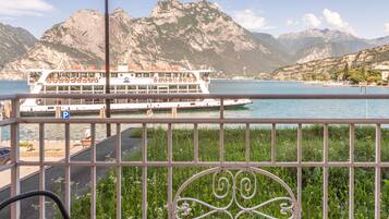 A balcony with metal railings and two chairs, overlooking a body of water with a cruise ship and mountains in the background.