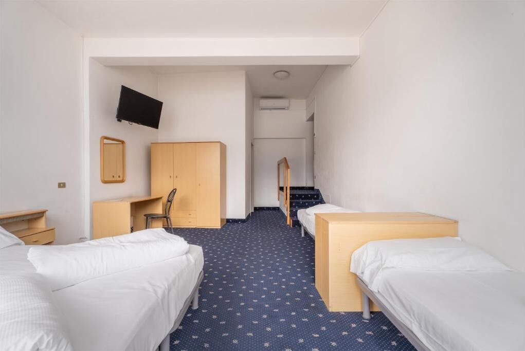 A hotel room with two single beds, a desk with a chair, a TV mounted on the wall, and a mirror.