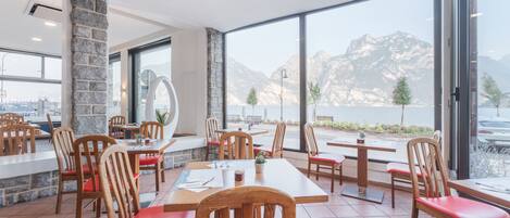 A restaurant with wooden tables and chairs, large windows with a mountain view, and a stone pillar.