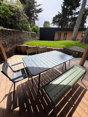 Relax on the patio with a table and chairs, surrounded by a lush lawn and a modern building.