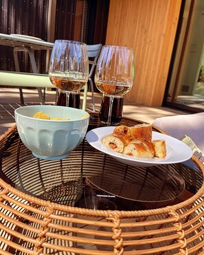 Guests can enjoy a meal at a wicker table with a glass top, featuring a plate with a sandwich and chips, accompanied by two wine glasses.