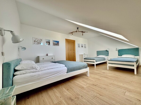 Een slaapkamer met twee bedden, een houten vloer en een schuin dak met dakraam.