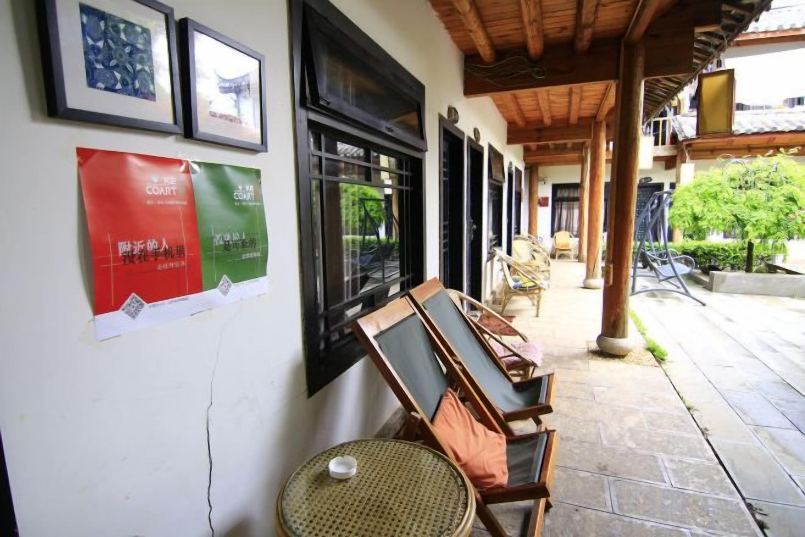 Un espacio al aire libre cubierto con sillas y mesas de madera, una pared decorada con cuadros y un cartel.