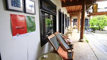 Un espacio al aire libre cubierto con sillas y mesas de madera, una pared decorada con cuadros y un cartel.