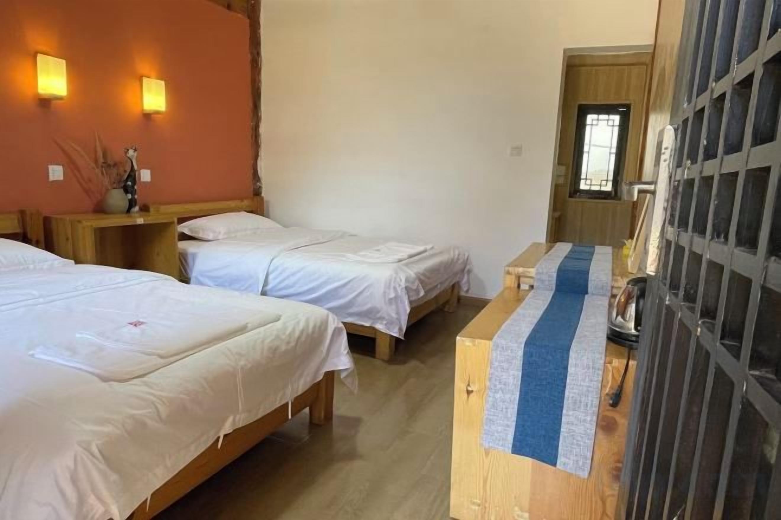 A room with three single beds, a wooden desk, and a small table with a blue and white striped tablecloth.