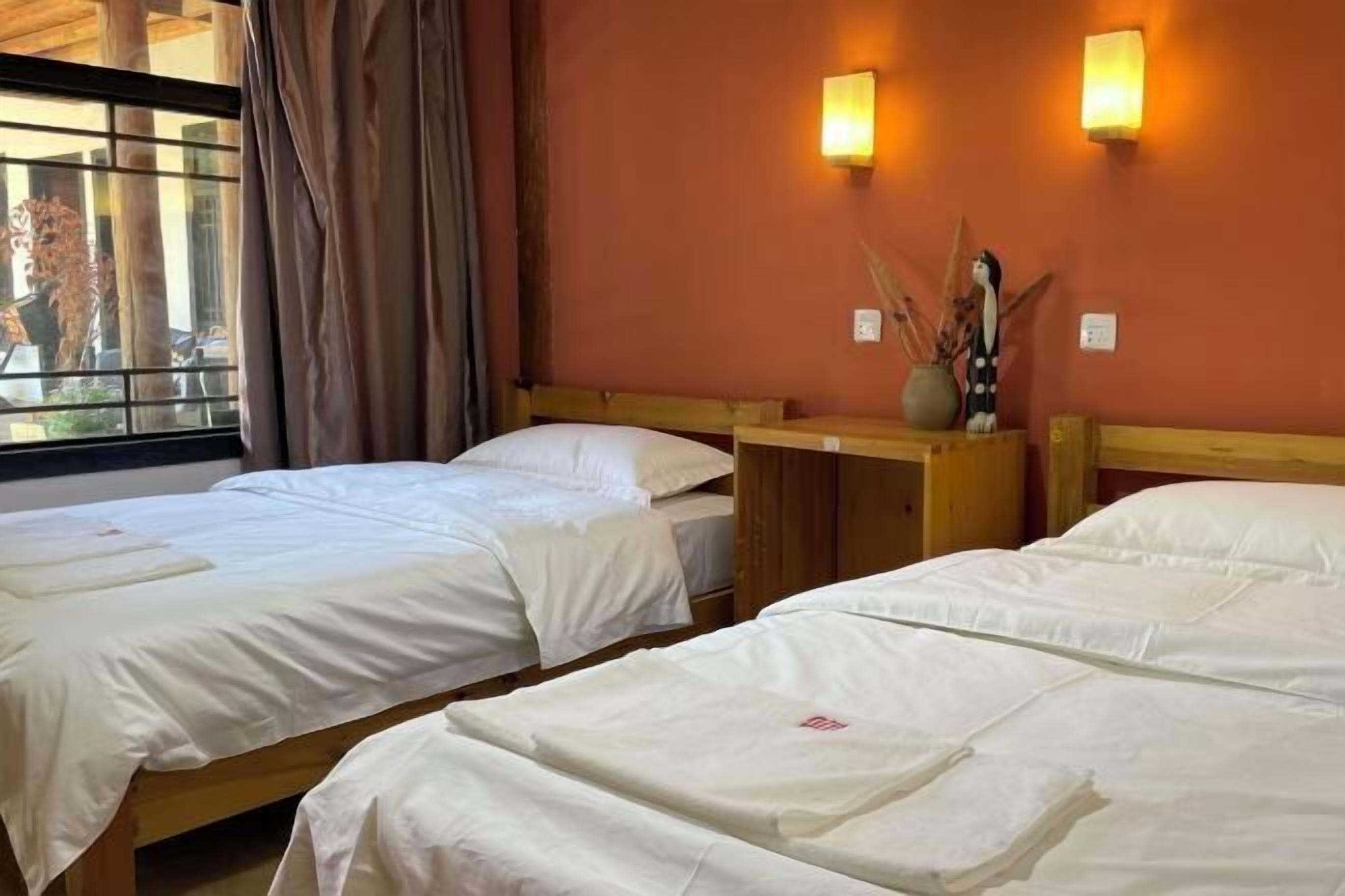 Ein Hotelzimmer mit zwei Einzelbetten, Holz-Kopfteilen und einem Fenster mit Vorhängen.