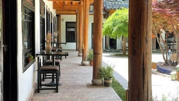 Un patio exterior con mesas y sillas, pilares de madera y plantas en macetas.