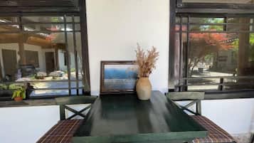 A table with a vase of dried plants, a framed picture, and a window with a view of a garden.