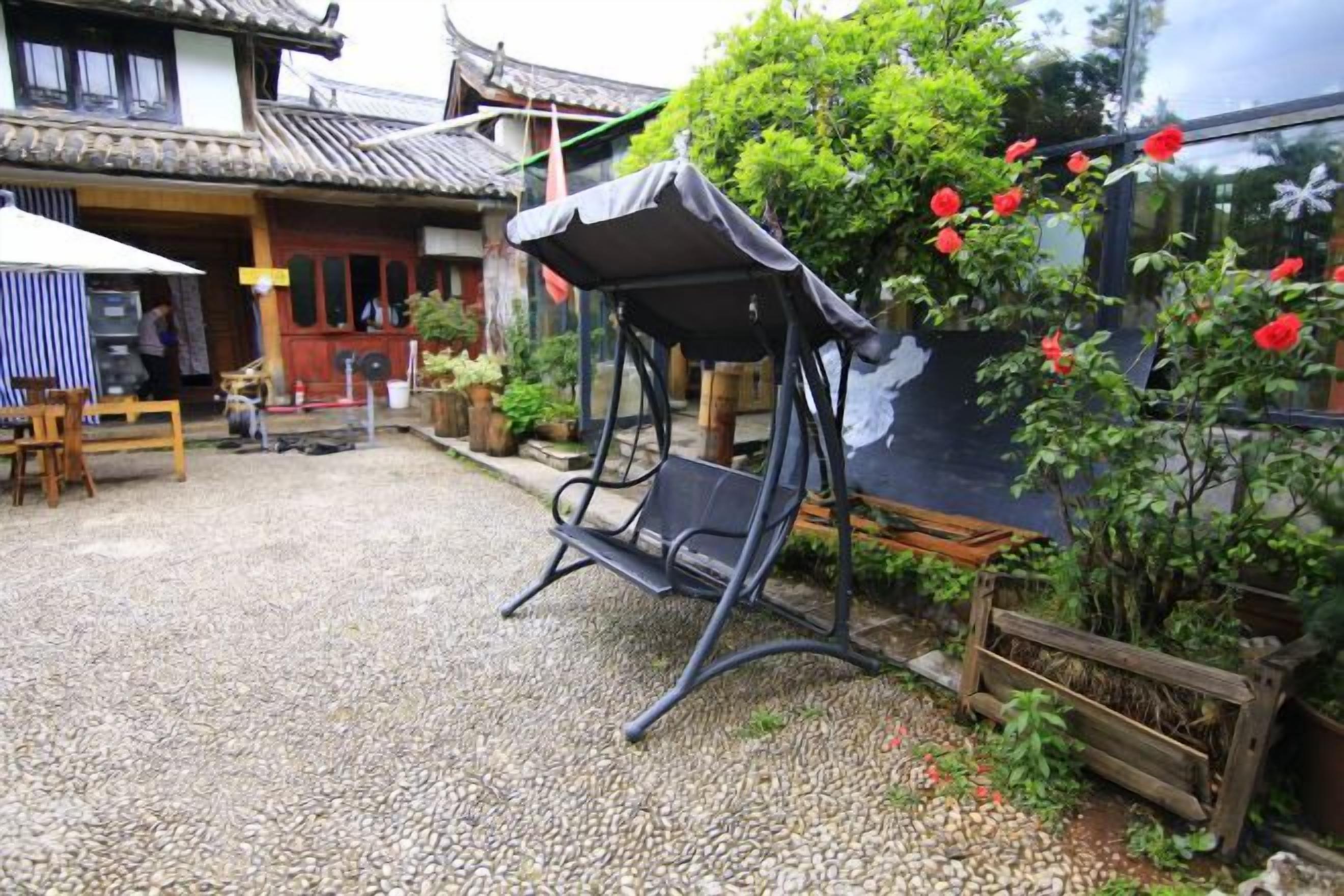 A traditional building with a tiled roof, a swing seat, and a garden with red flowers.