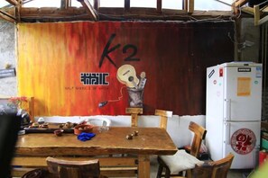 A rustic dining area with a wooden table, chairs, and a refrigerator. - Lijiang Shuhe K2 International Youth Hotle (Lijiang)