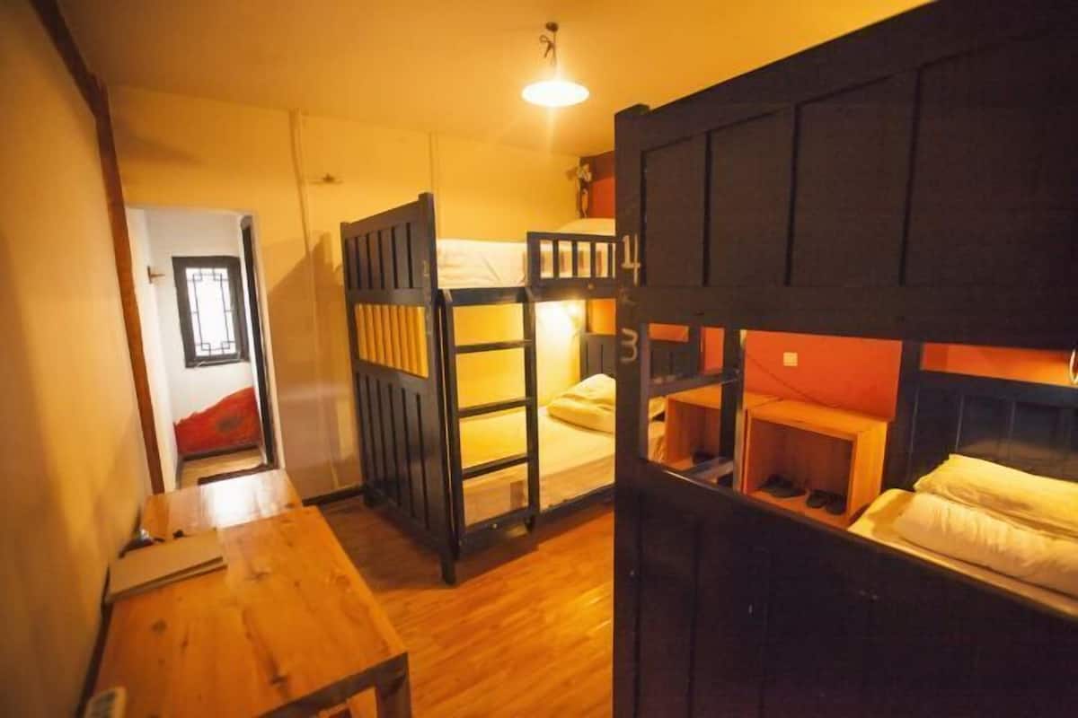 A dormitory-style room with bunk beds, a wooden table, and a door leading to another room.