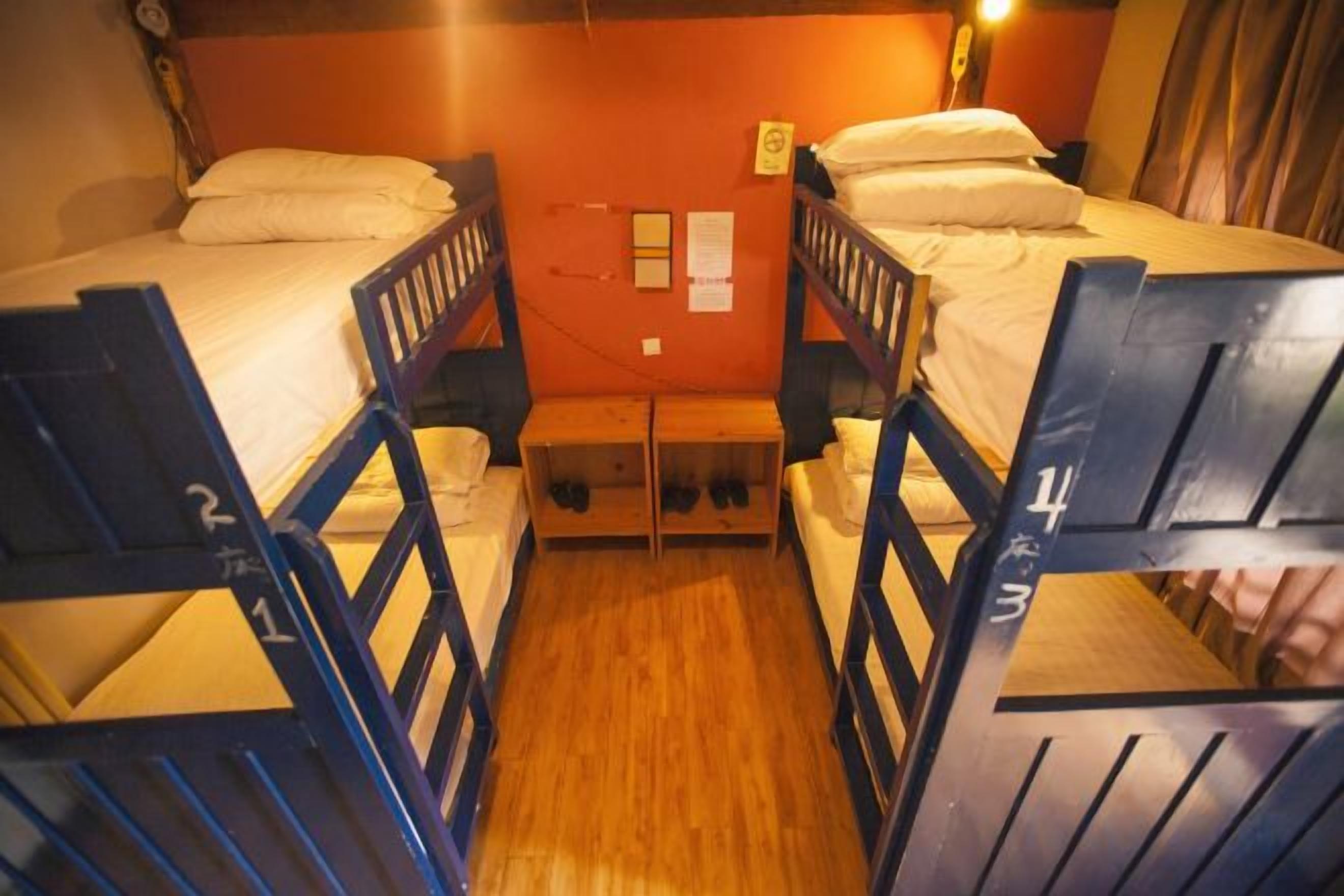 A dormitory room with bunk beds, a wooden bench, and a small table.