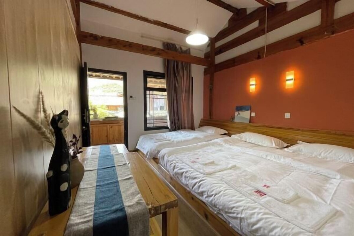 Habitación con dos camas, vigas de madera, un banco y una decoración de panda, con vistas al exterior.