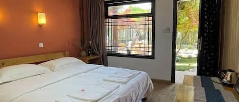 A bedroom with a bed, a window with a view of the outdoors, and a door leading to a balcony.