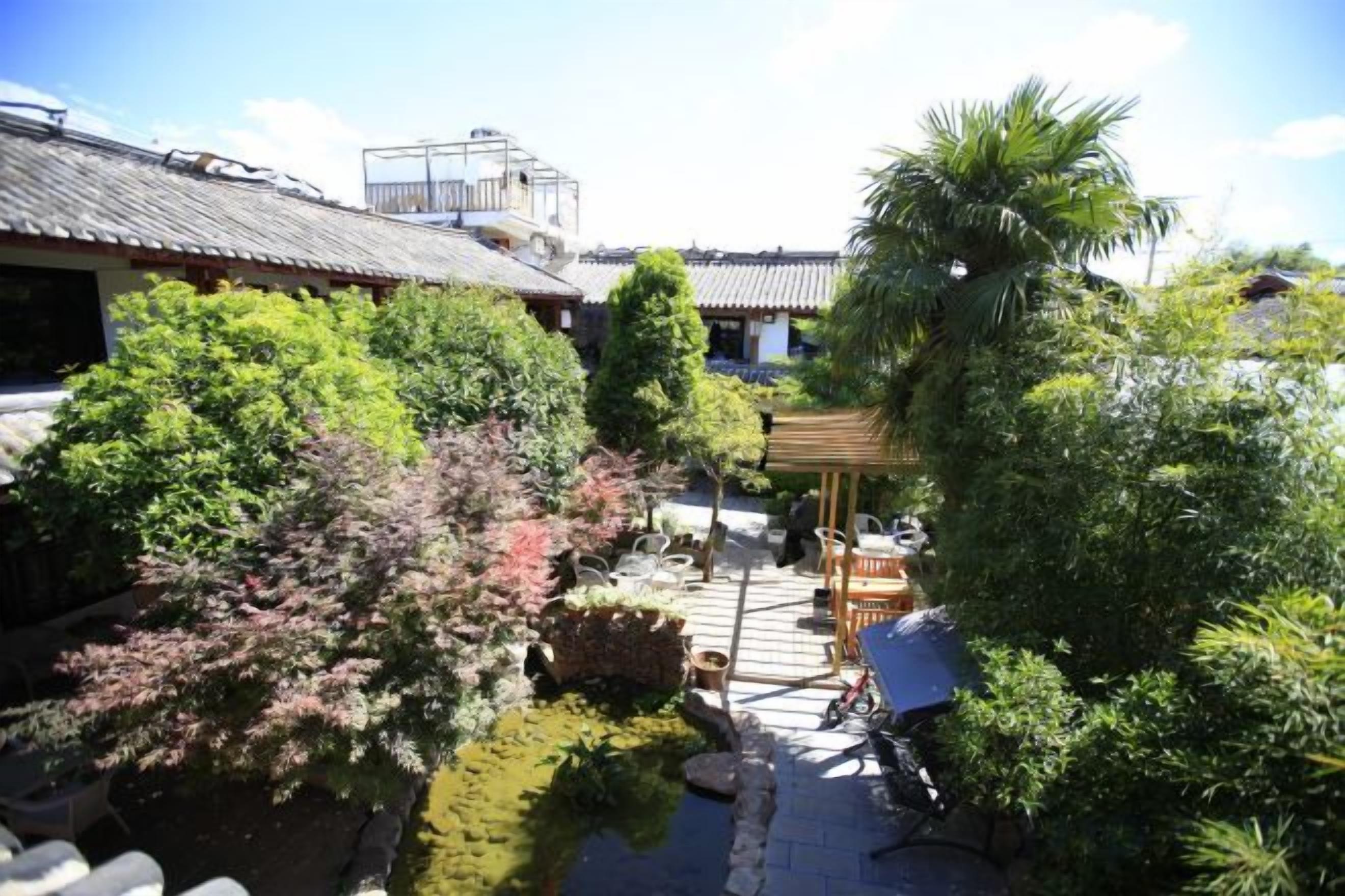 A traditional Japanese garden with a wooden structure, a small pond, and various trees.