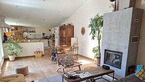 Ein großzügiger Wohnbereich mit einer Couch, einem Couchtisch und einem Kamin. Im Hintergrund ist eine Küche mit Essbereich zu sehen.