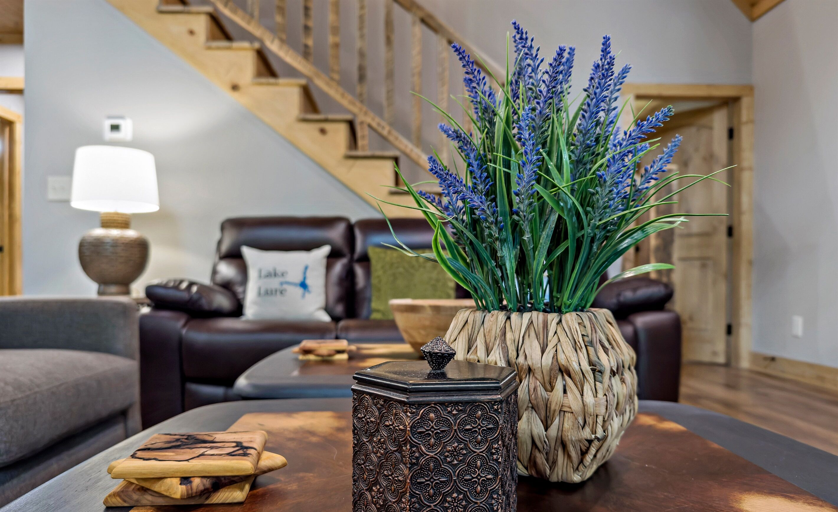 A living room with a sofa, a coffee table with decorative items, a staircase, and a wall-mounted lamp.