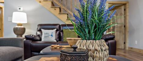 A living room with a sofa, a coffee table with decorative items, a staircase, and a wall-mounted lamp.