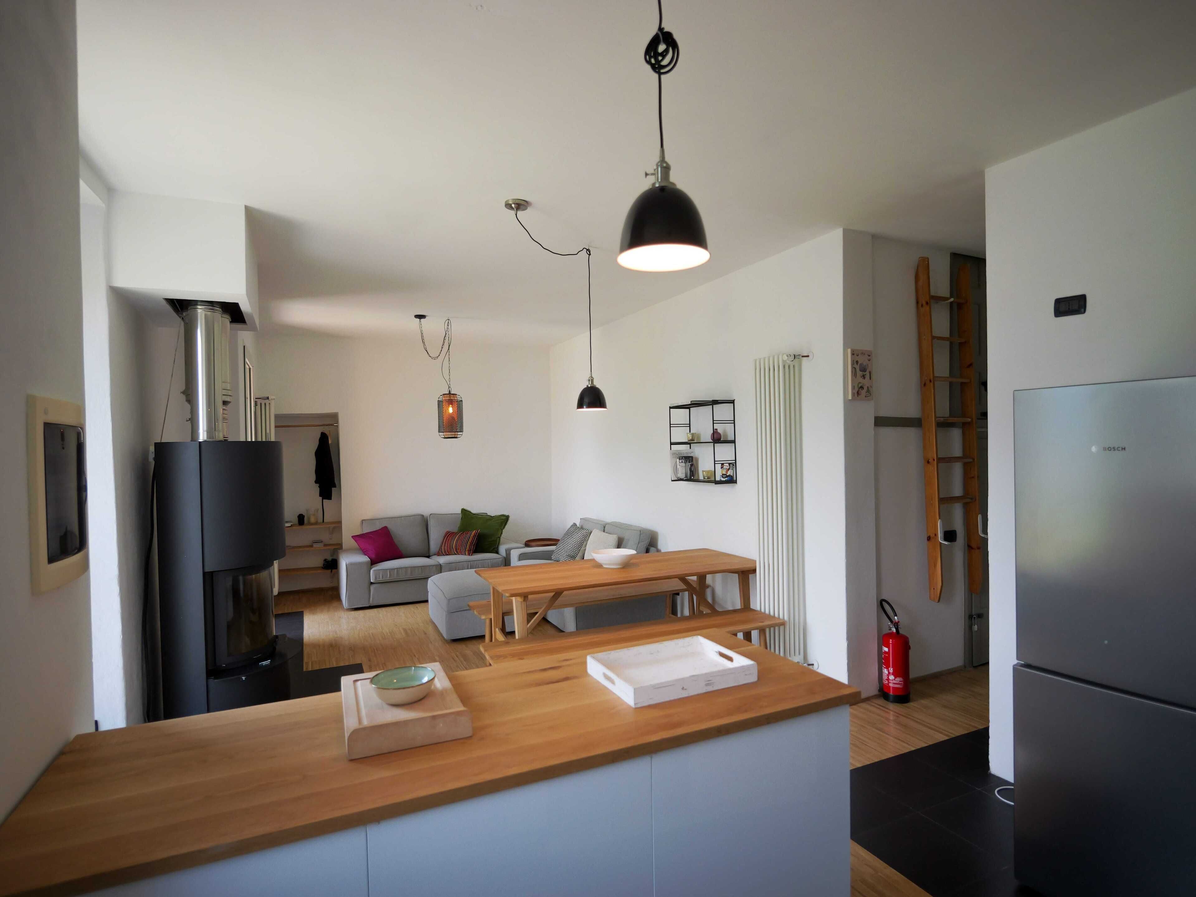 Una cocina moderna con una isla de madera, horno empotrado y refrigerador. Hay un comedor con mesa y sillas, y una sala de estar con sofá y mesa de centro.