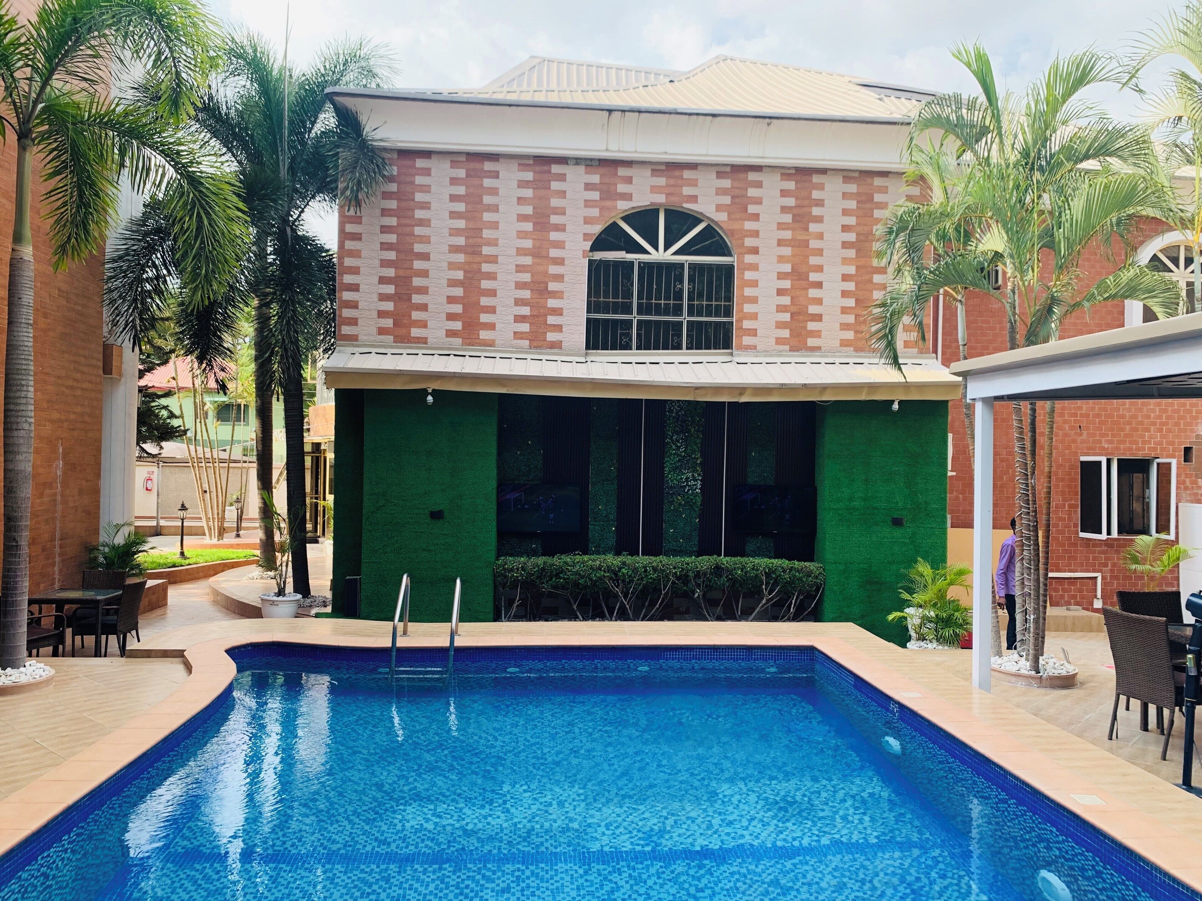 A swimming pool with a clear blue water surface, surrounded by a brick building with a green facade and a large arched window.