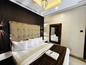 A hotel room with a large bed, a headboard, a bedside table, a mirror, and a wall-mounted light fixture.
