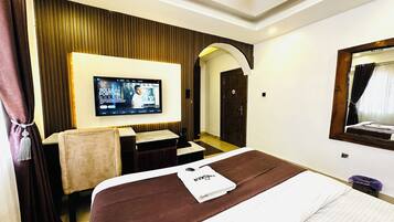 Habitación de hotel con una cama grande, televisor montado en la pared, escritorio y puerta.